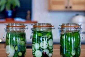 Drei Gläser mit eingelegten Gurken und anderem Gemüse auf einer Küchenarbeitsplatte